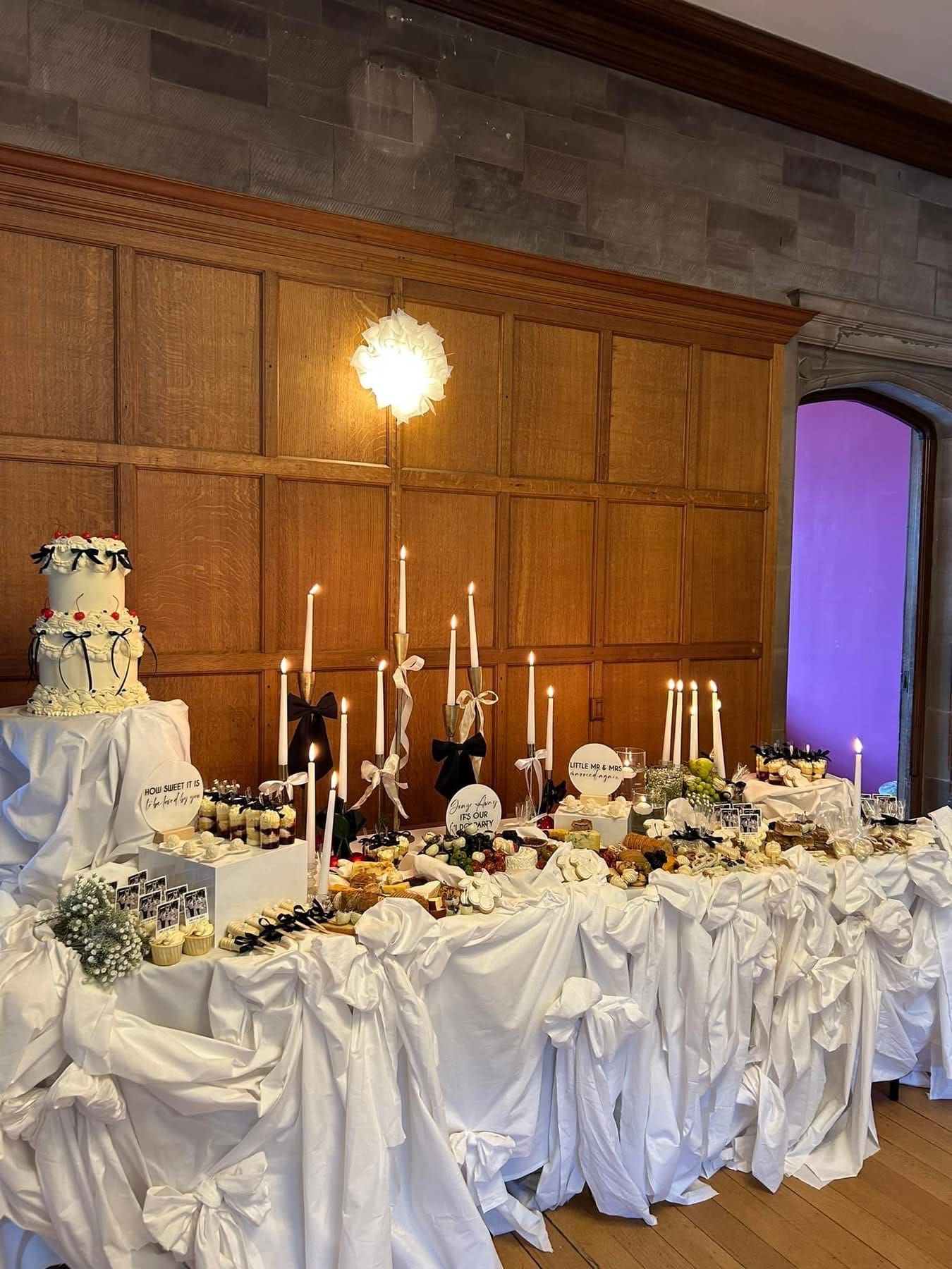 A wedding grazing table set up with white bow tablecloth, candles, and an array of grazing food.