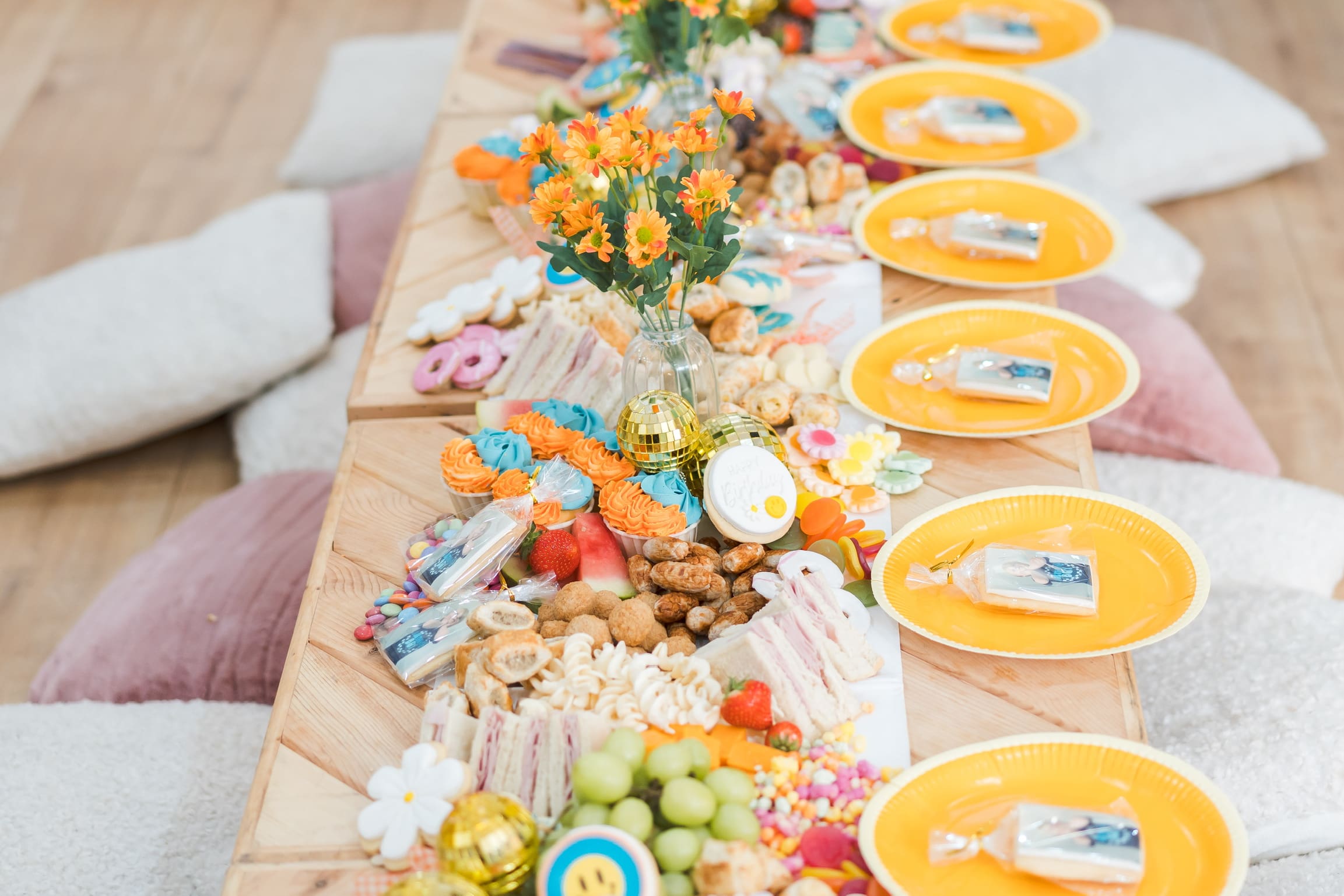 A long grazing table for a child'd birthday party, featuring plates and party favours, flowers and a display of grazing food.